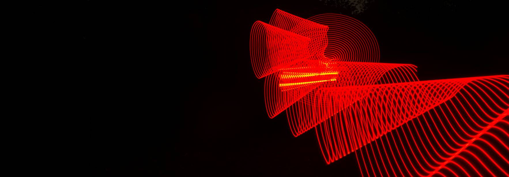 La imagen muestra un patrón de luces rojas en movimiento sobre un fondo oscuro.