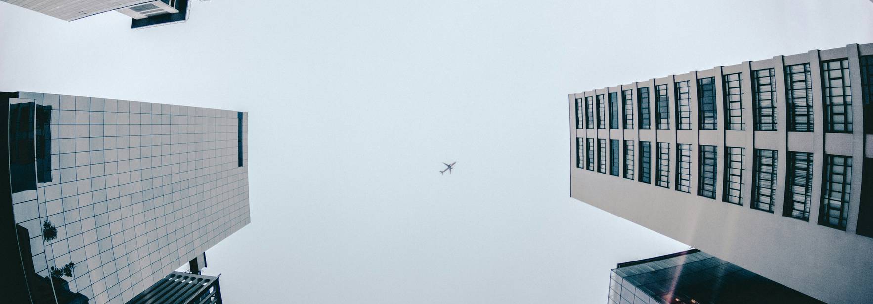 Una vista desde el suelo hacia arriba, con edificios altos y un avión en el cielo.