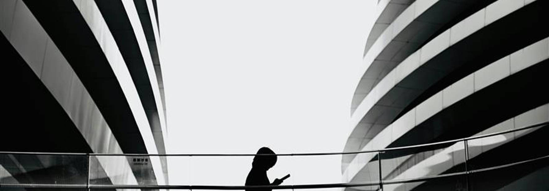 Una silueta de una persona con capucha caminando entre dos estructuras arquitectónicas modernas.