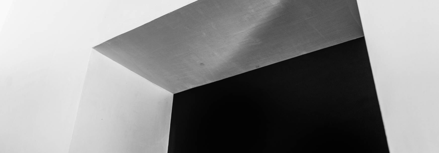 La imagen muestra un ángulo de una pared con un marco en la parte superior iluminado en blanco y un fondo negro.