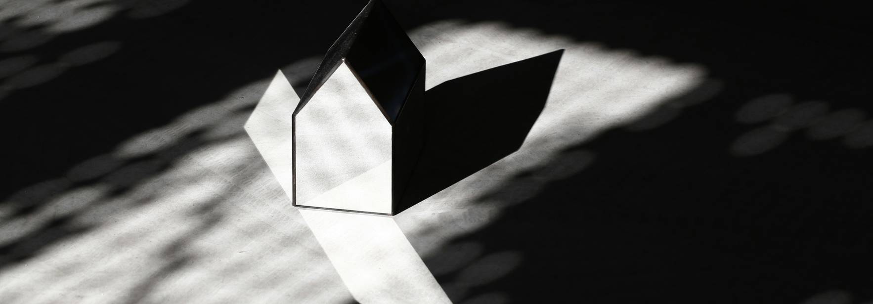Un objeto en forma de casa proyecta su sombra sobre una superficie iluminada por sombras en patrón.
