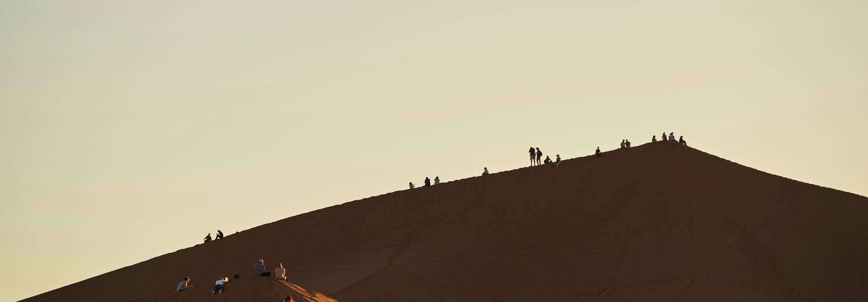 Una escena desértica con personas en las dunas al atardecer.