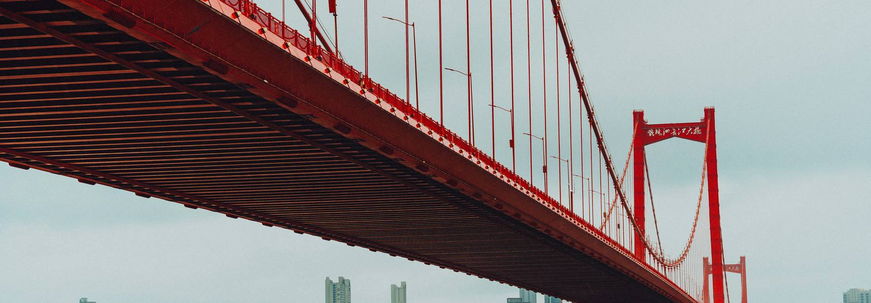 Un puente rojo se extiende sobre la ciudad con rascacielos de fondo.