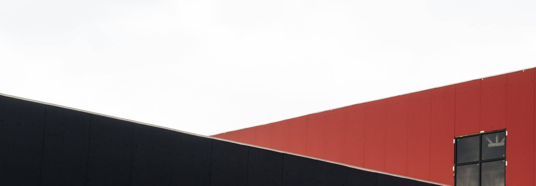 La imagen muestra una pared roja y negra de un edificio con un cielo nublado de fondo.