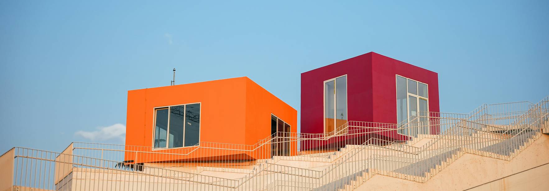 Dos casas coloridas, una naranja y otra morada, se encuentran en una colina con un cielo azul claro de fondo.