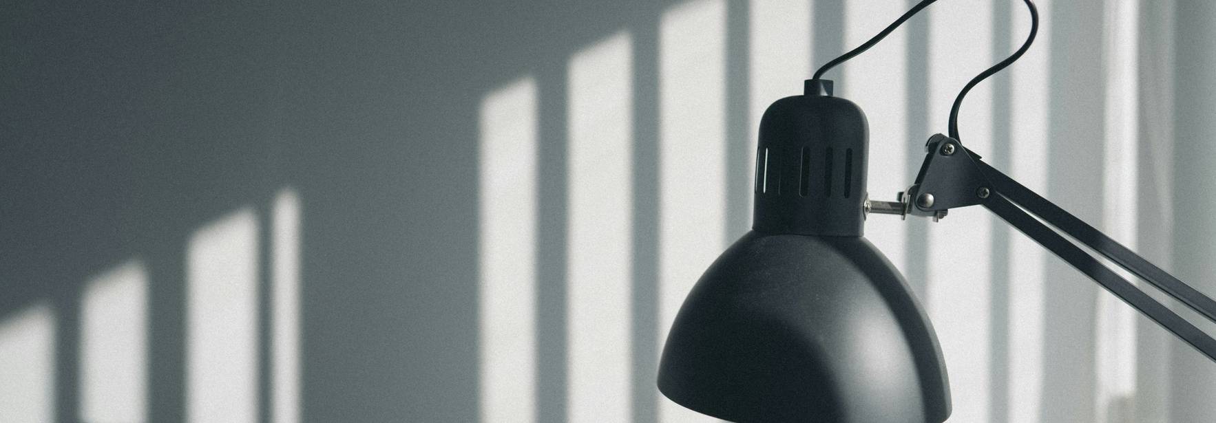 Una lámpara negra emite luz mientras proyecta sombras en la pared.