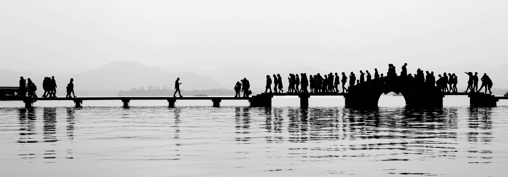 Silhuetas de personas caminando sobre un puente en un entorno neblinoso.