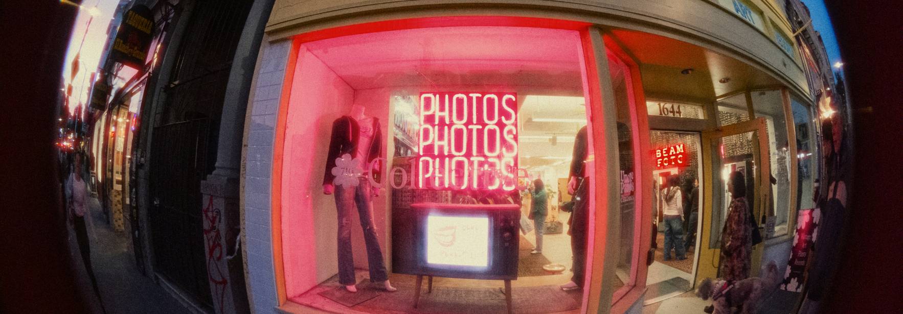 Una tienda vintage con un escaparate iluminado en rosa, mostrando el texto 'PHOTOS'.