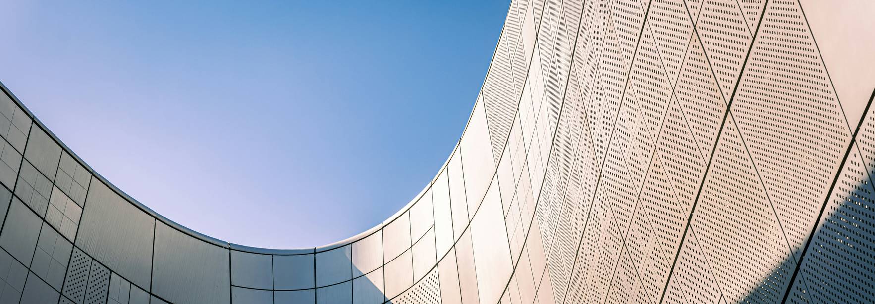La imagen muestra una vista desde abajo de una estructura arquitectónica moderna con paredes curvas y un cielo azul de fondo.