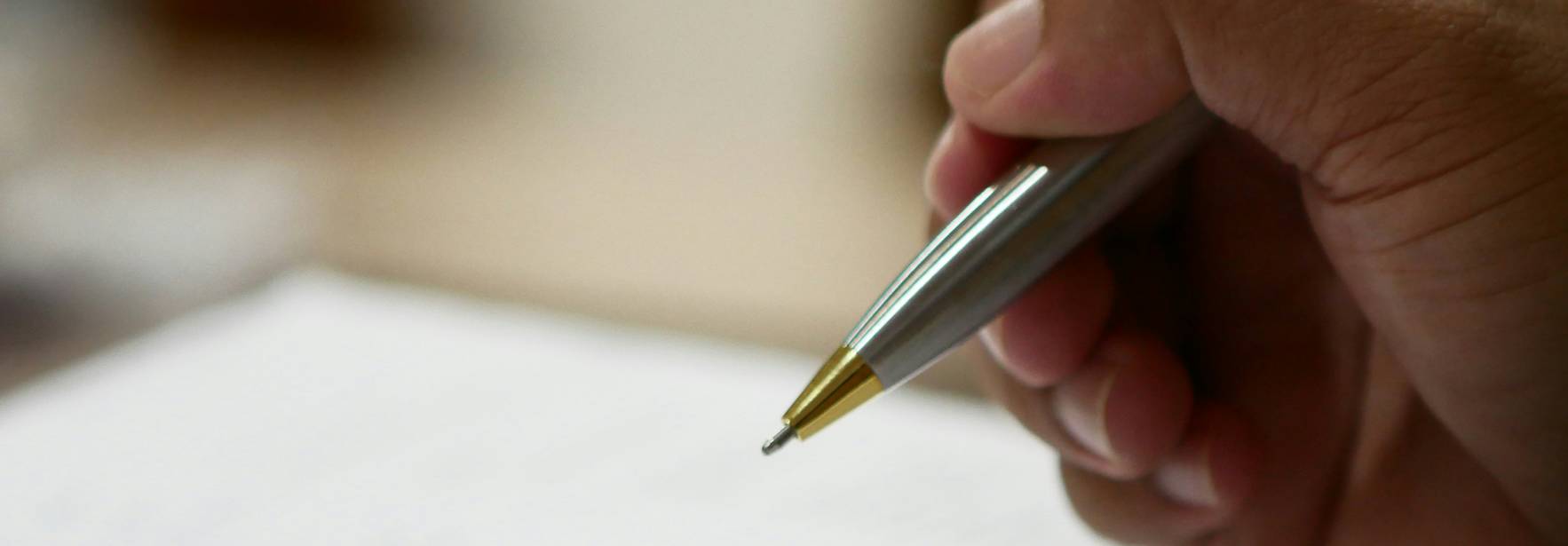 Una mano sostiene un bolígrafo mientras escribe en una hoja de papel con varias columnas y líneas.