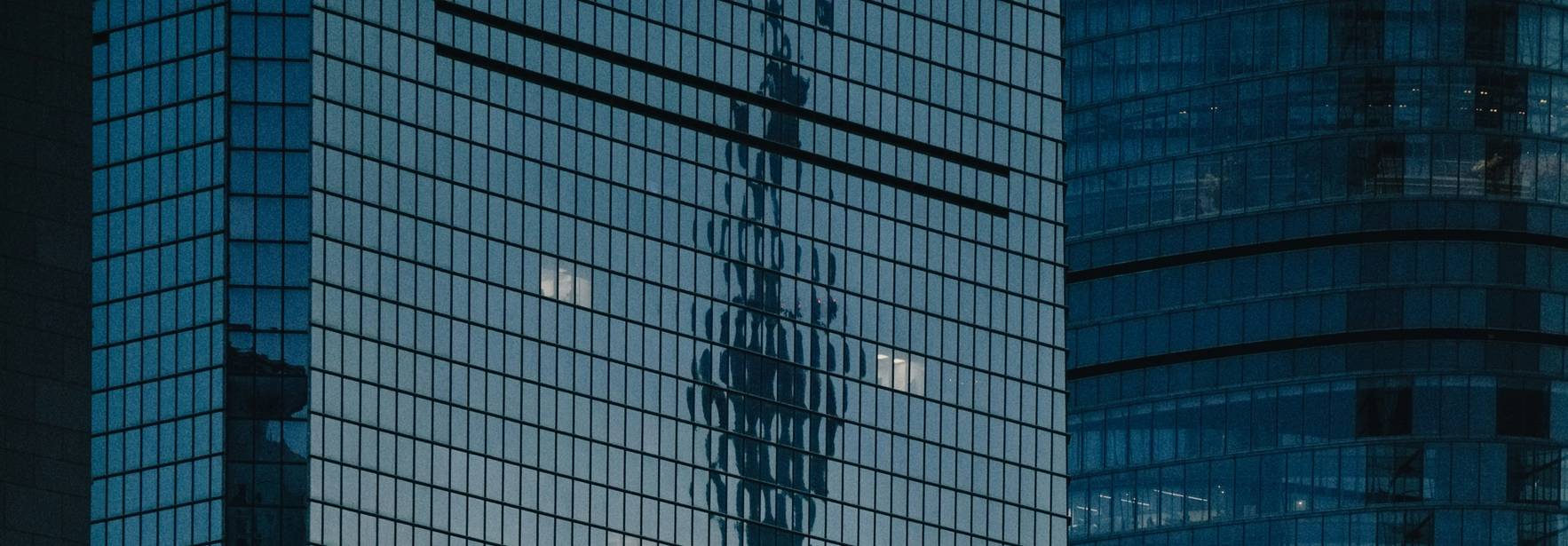 La imagen muestra el reflejo de una torre en los ventanales de un edificio moderno.