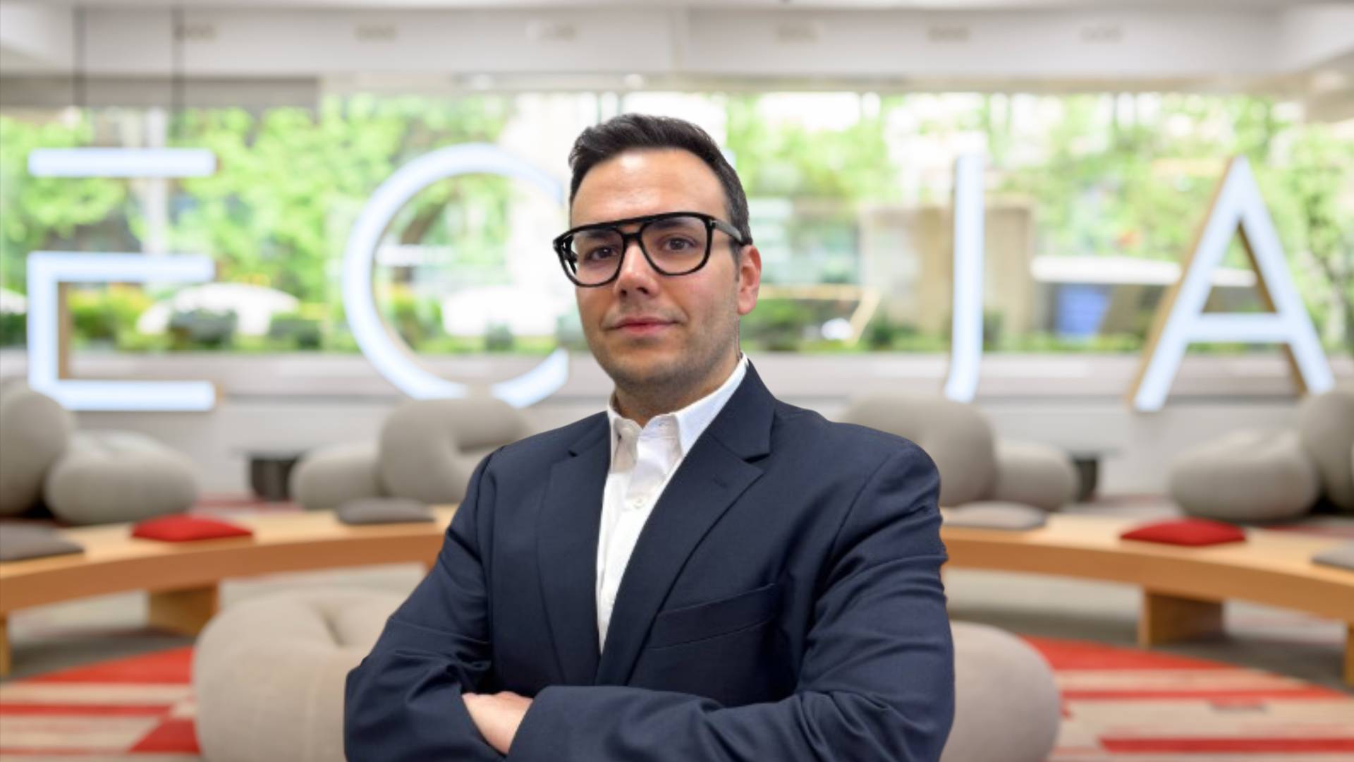 Un hombre de negocios con gafas de alta graduación posando en un entorno moderno y profesional.