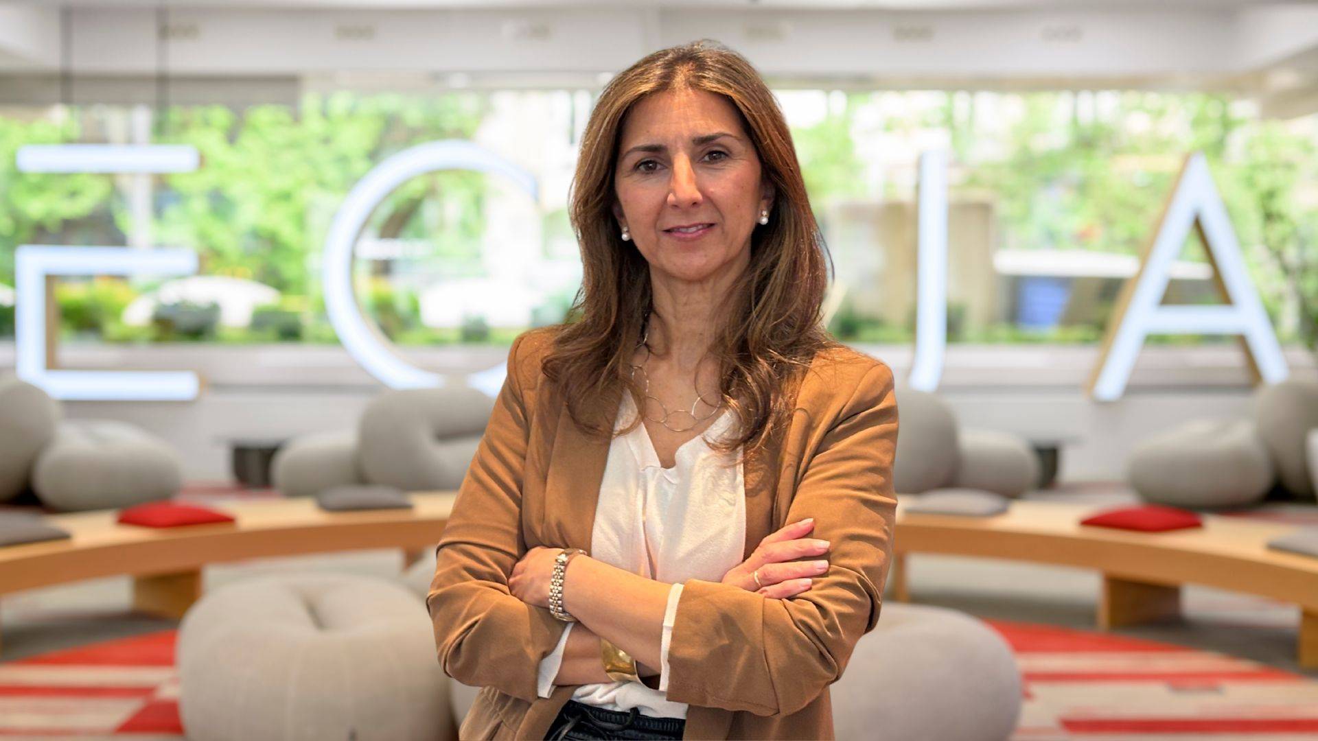 Mujer de pie frente a un fondo que muestra el nombre de la empresa en un ambiente moderno y luminoso.