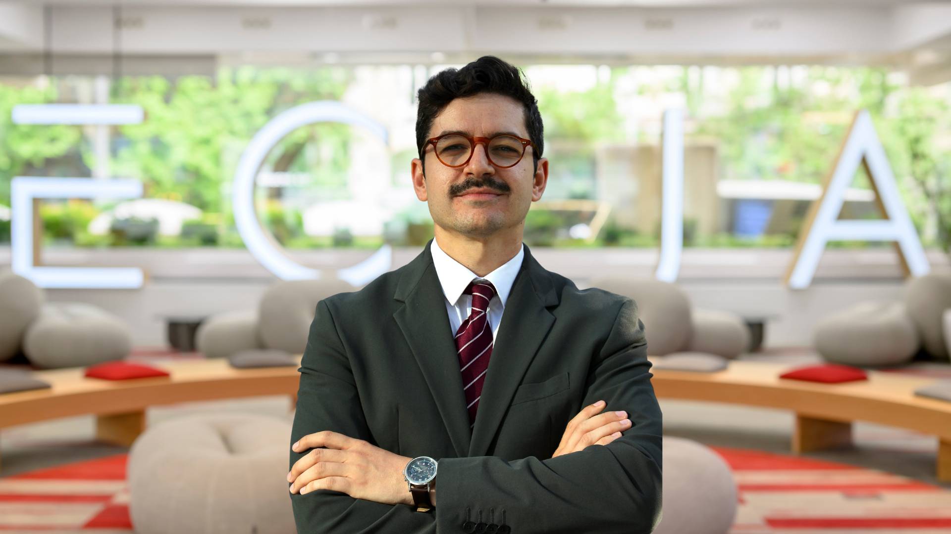 Hombre de pie con bufanda y traje frente a un fondo moderno y minimalista.
