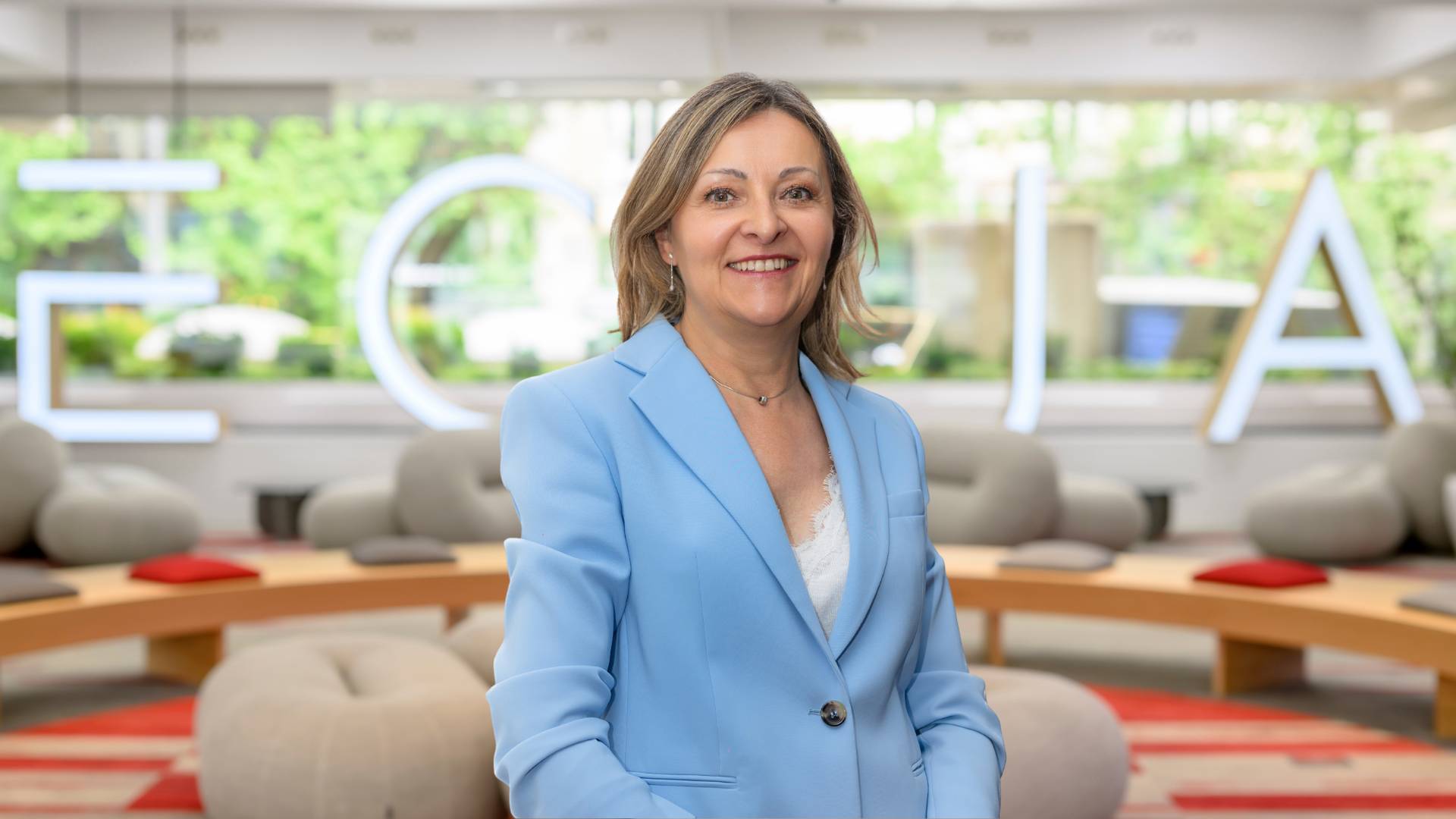 Una mujer sonriente con un blazer azul posando en un entorno moderno y luminoso.