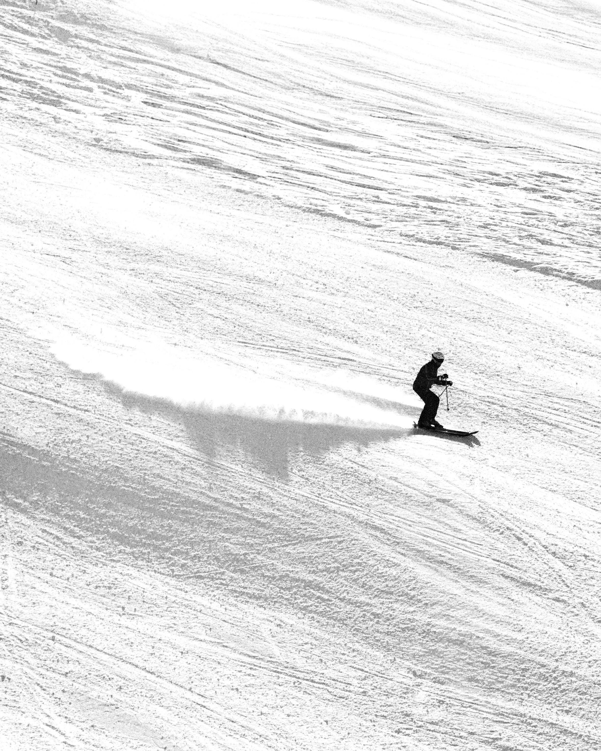 Un esquiador desciende por una pista nevada dejando una estela de nieve.