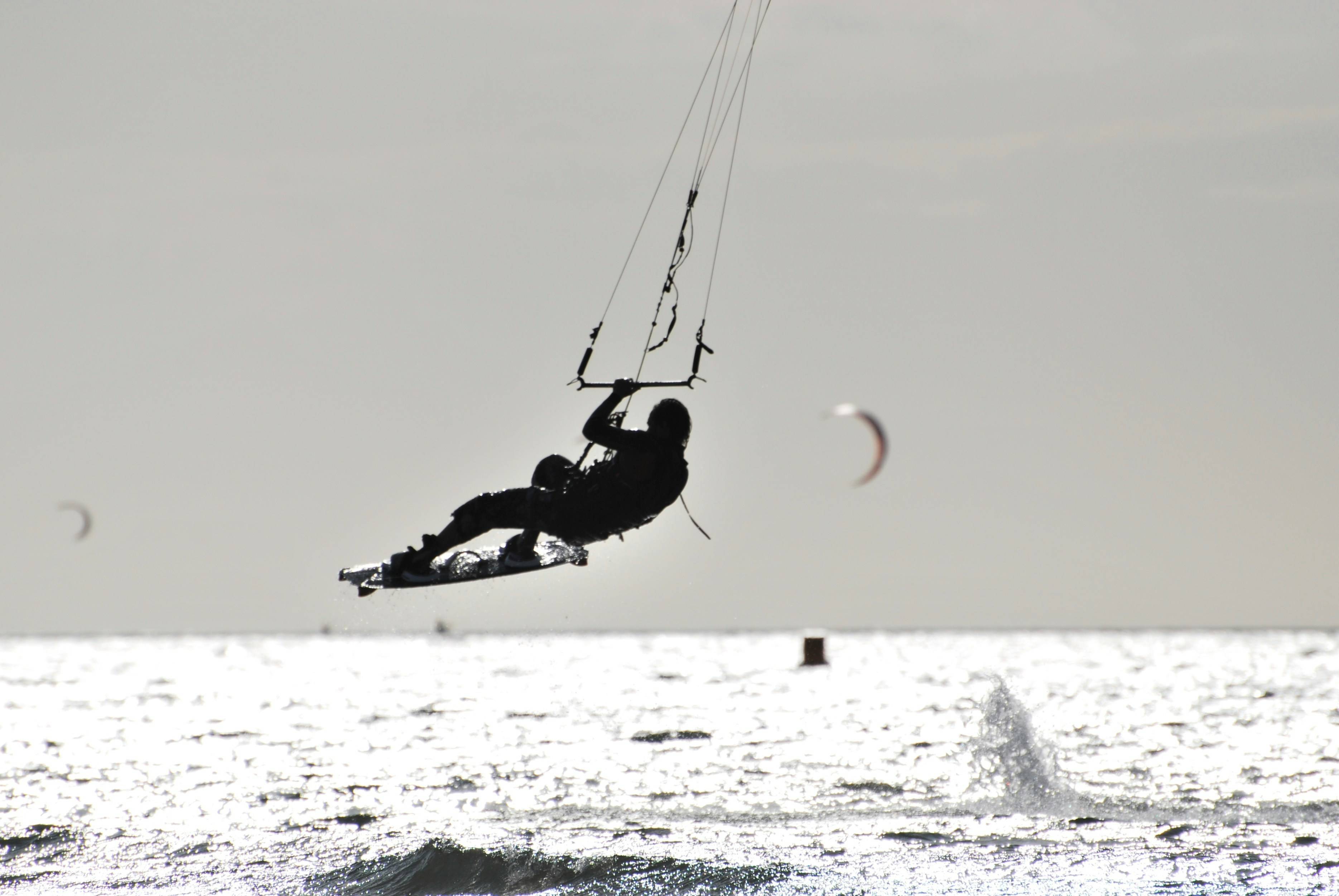 Una persona practicando kitesurf en el mar con varias cometas al fondo.
