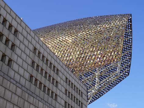 La imagen muestra un edificio moderno con una estructura arquitectónica distintiva en tonos dorados y plateados.