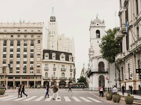 Vista de un cruce peatonal en una ciudad con edificios históricos y múltiples peatones cruzando la calle.
