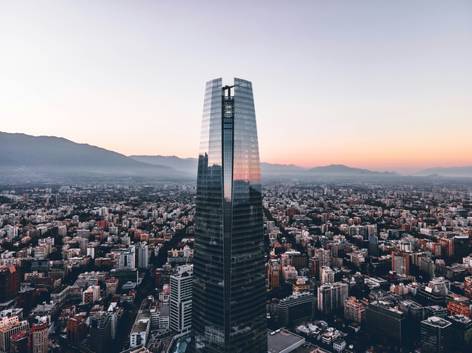 Vista aérea de una ciudad moderna al atardecer, destacando un rascacielos de vidrio en primer plano.