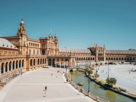 La imagen muestra la Plaza de España en Sevilla, un emblemático monumento innovador con arquitectura neomudéjar y un canal que la rodea.