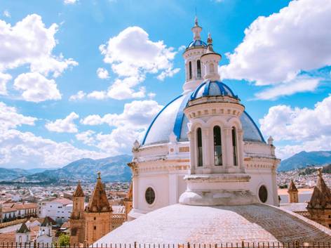 Vista de una cúpula blanca y azul de una iglesia con la ciudad de fondo bajo un cielo claro.