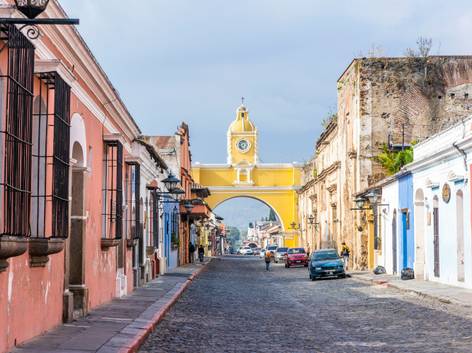 Vista de una calle empedrada con casas coloridas y un arco amarillo al fondo bajo un cielo nublado.