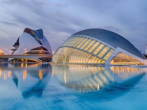 Vista del complejo arquitectónico moderno con estructuras futuristas reflejadas sobre un cuerpo de agua al atardecer.