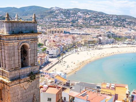 Vista panorámica de una ciudad costera con una playa y un antiguo campanario en primer plano.