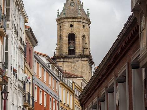 Una calle empedrada con edificaciones coloridas y una torre de iglesia al fondo bajo un cielo nublado.