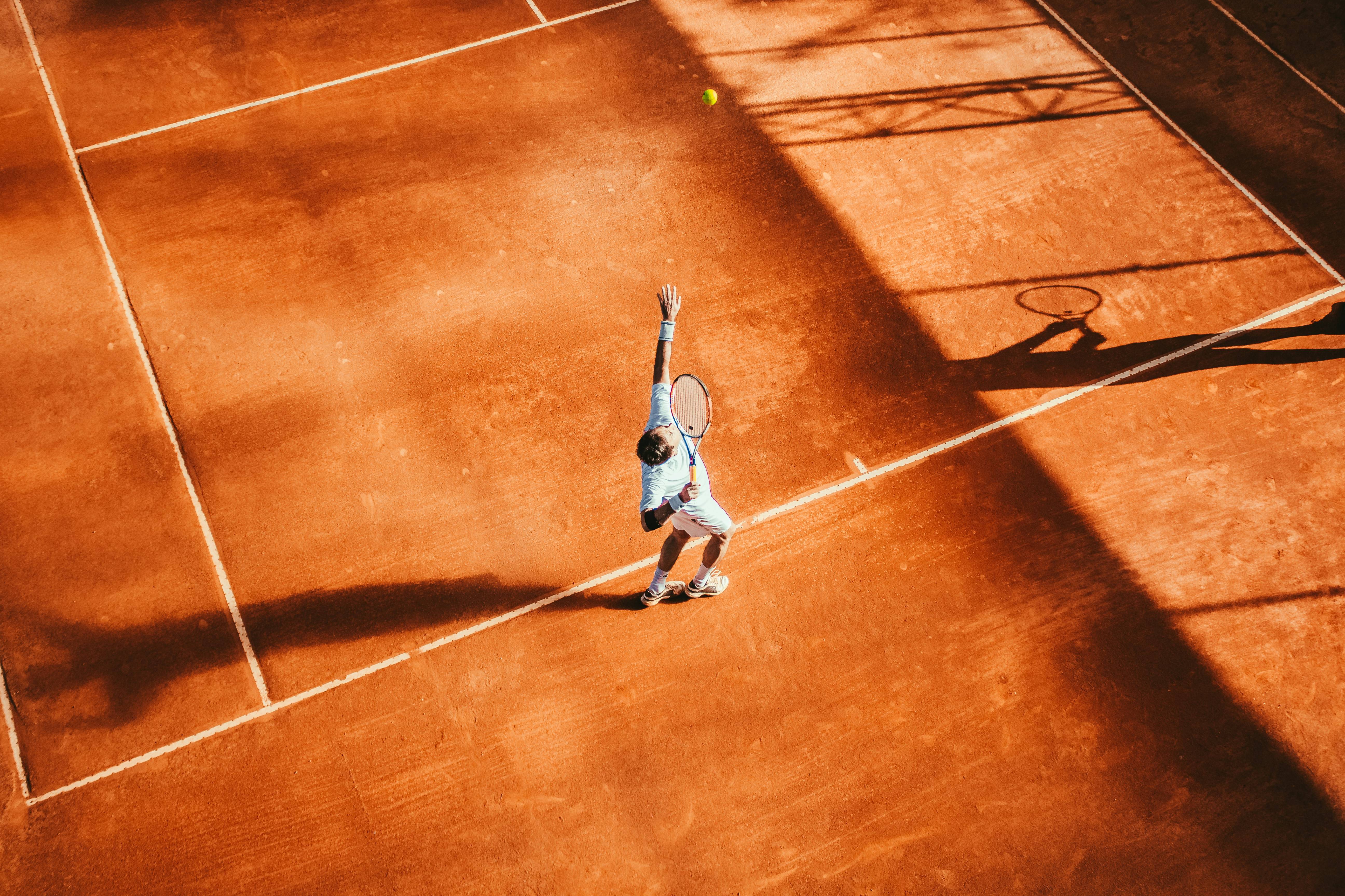 Un jugador de tenis sirve la pelota en una cancha de tierra batida.