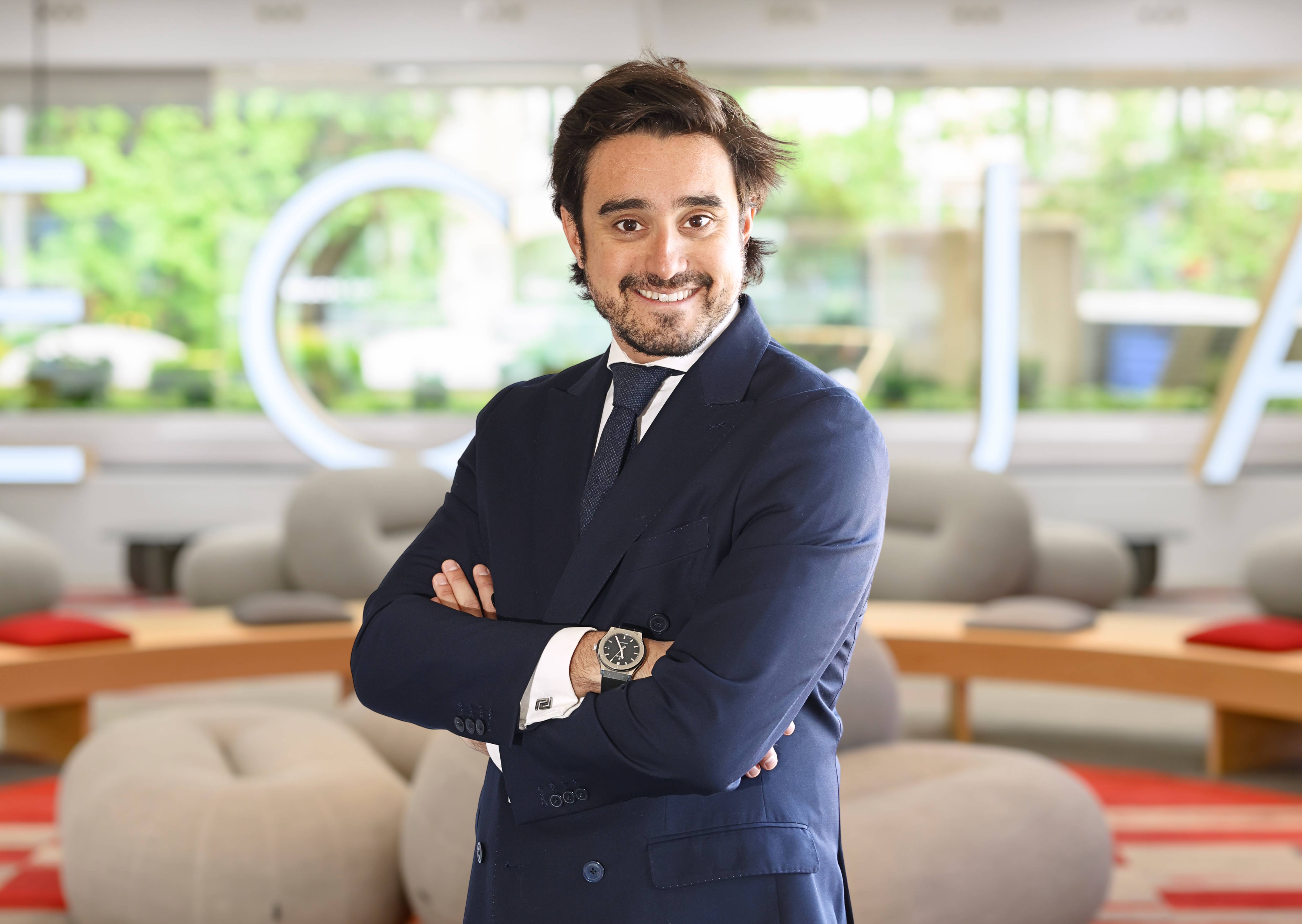 Un hombre sonriente con traje formal posando en un ambiente moderno.