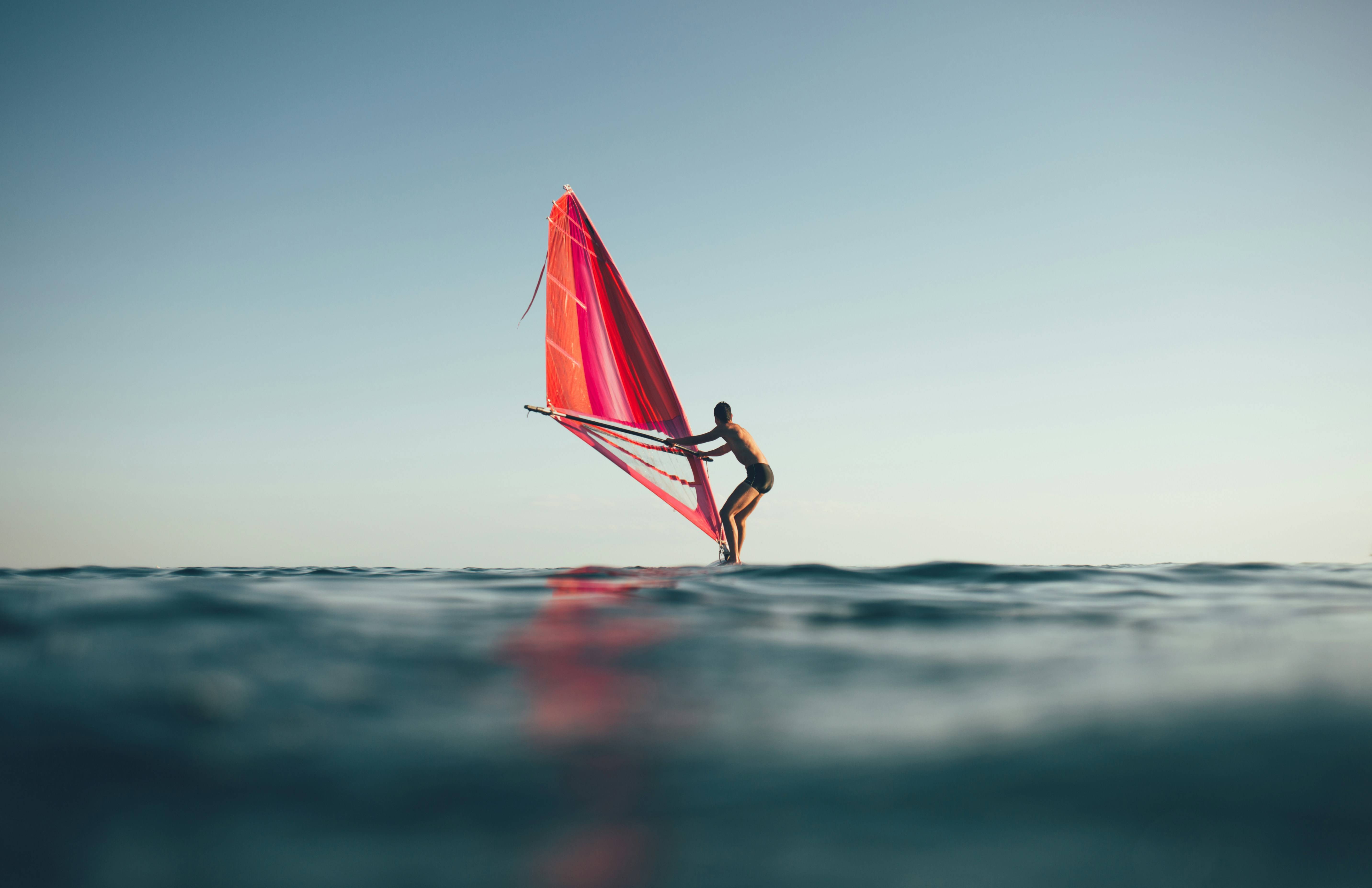 Una persona está practicando windsurf en el mar con una vela roja.