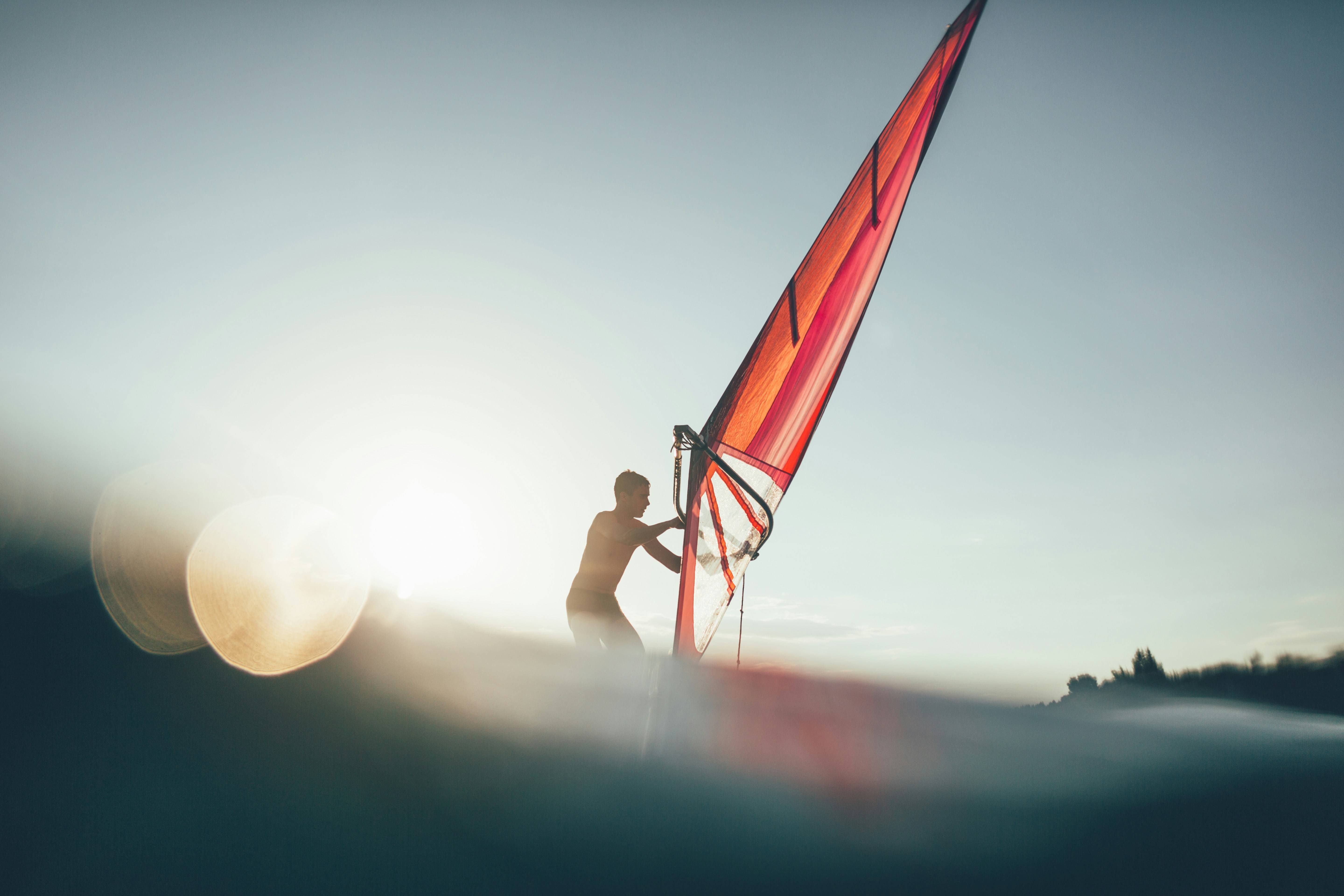 Un hombre navegando en una tabla de windsurf al atardecer.