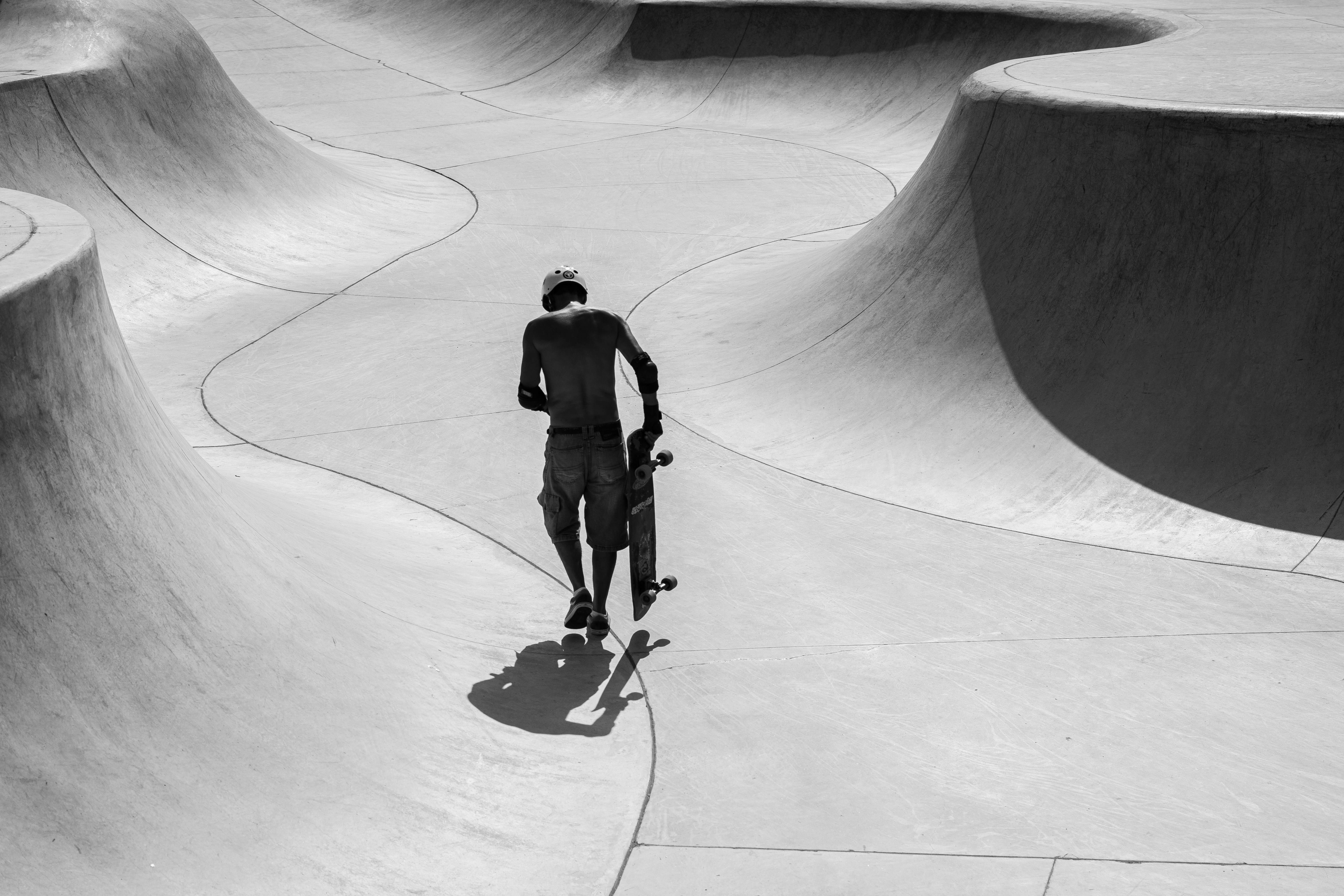 Un skater camina por un parque de patinaje vacío y curvado.