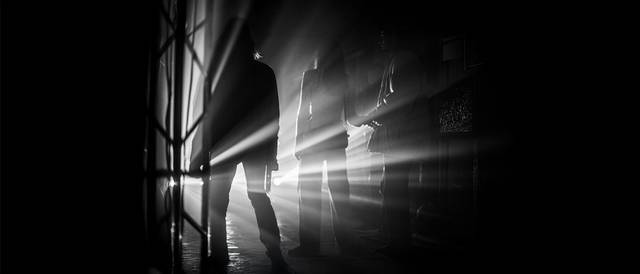 La imagen muestra siluetas de personas iluminadas por rayos de luz en un ambiente oscuro.