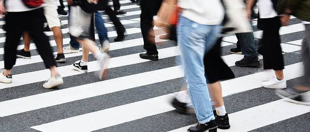 Una multitud de personas cruza una calle con rayas blancas y negras.