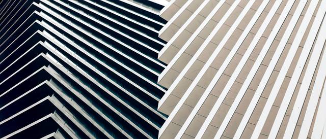 La imagen muestra un edificio con una fachada compuesta de líneas horizontales que alternan entre colores oscuros y claros.