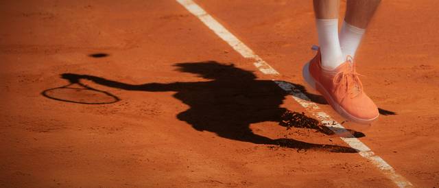 Un jugador de tenis en acción sobre una cancha de tierra batida que se prepara para golpear la pelota.