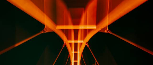 La imagen muestra un puente iluminado con luces de tono naranja contra un fondo oscuro.