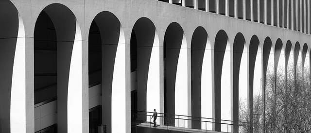 Una persona camina bajo una estructura arquitectónica con arcos en blanco y negro.
