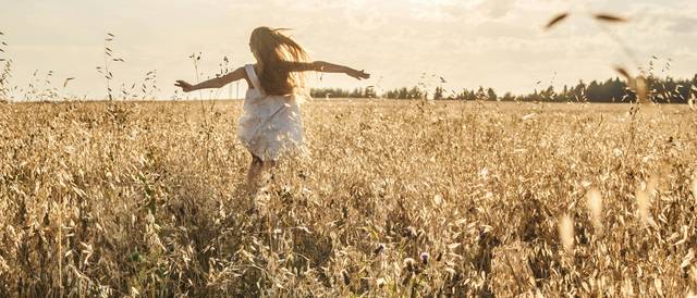 Una niña corre libremente por un campo dorado bajo el sol radiante.