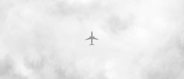 Un avión vuela entre las nubes en un cielo gris.