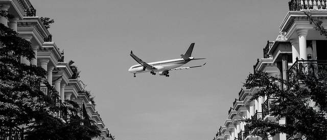 Un avión vuela entre edificios en un ambiente urbano teñido de blanco y negro.
