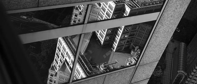La imagen muestra un reflejo arquitectónico en blanco y negro de un edificio en la superficie de otro edificio.
