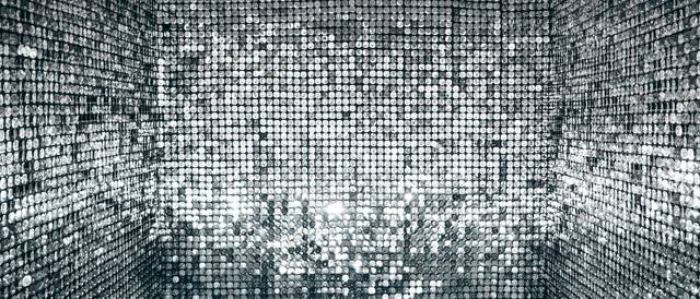 La imagen muestra un ambiente cubierto de superficies brillantes que reflejan luces en patrones deslumbrantes.