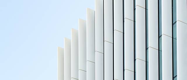 La imagen muestra una fachada de edificio con paneles verticales y un cielo azul de fondo.