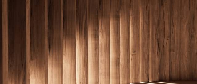 La imagen muestra un espacio interior con columnas de madera iluminadas suavemente y sombras alargadas en el suelo.