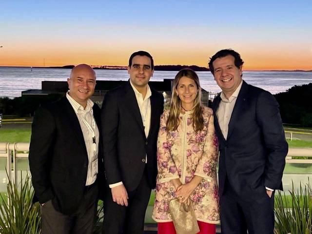 Cuatro personas posan juntas frente a un paisaje con un atardecer junto al mar.