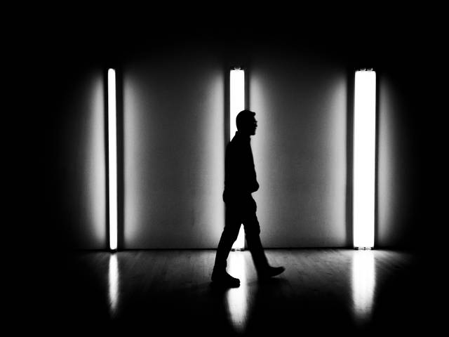 Una silueta de una persona caminando frente a luces brillantes en un espacio oscuro.